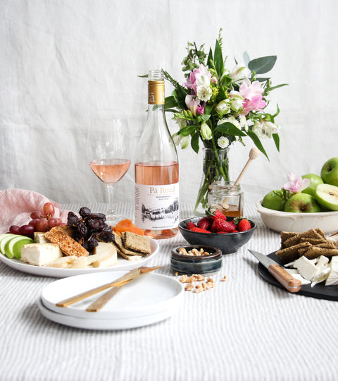 Image of Pa Road Rose wine on a white table, with cheese platters and flowers